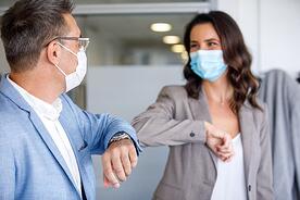 Two professional touching elbows wearing masks to show solidarity without spreading germs or viruses