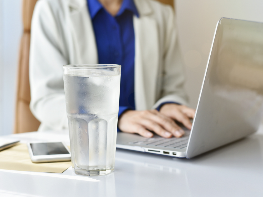 a businesswoman working at a laptop with a tall glass of cold water in the foreground