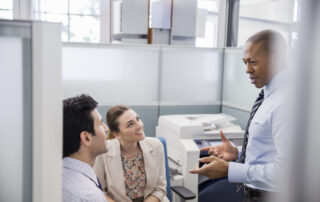 Businessman having a conversation with young professionals in an office cubicle with a business printer in the background