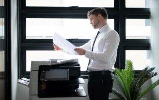 A professional stands in front of a laser printer in a Charlotte office examining the output with a questioning expression.
