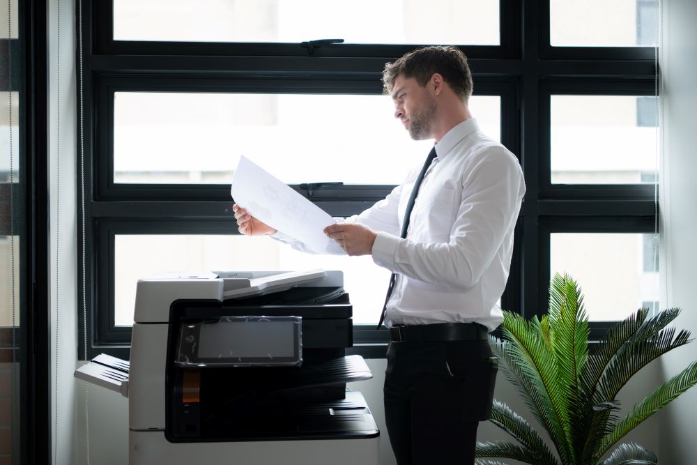 A professional stands in front of a laser printer in a Charlotte office examining the output with a questioning expression.