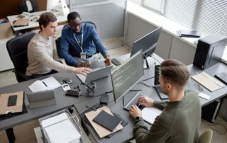 A team of IT professionals collaborating in a modern office, working on multiple screens with coding and data management, representing Managed IT Services.